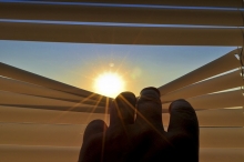 Hand peeking through blinds at sun
