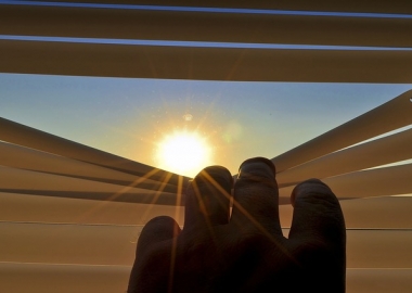 Hand peeking through blinds at sun