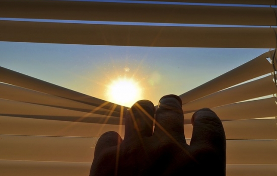 Hand peeking through blinds at sun