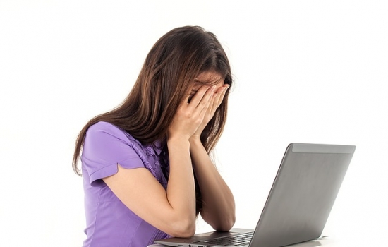 Woman with laptop and head in hands