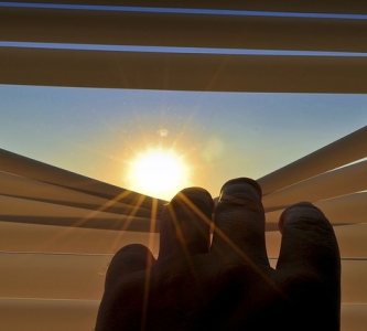 Hand peeking through blinds at sun